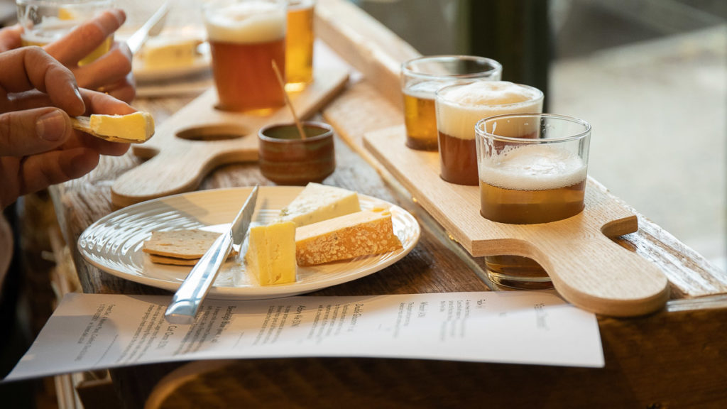 A selection of cheeses on a plate with a beer flight paddle